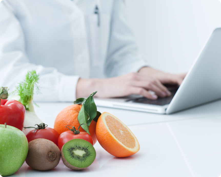 果物とパソコンで作業する医療従事者の写真。栄養指導をイメージ