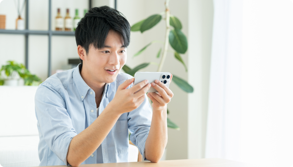 スマートフォンを手に笑顔で見つめる男性の写真