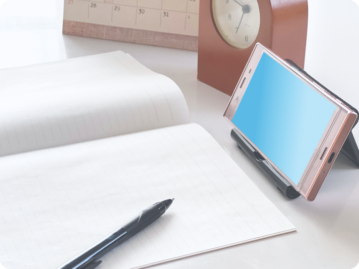 開かれたノートとペン、スマートフォンが置かれたデスク。学習環境のイメージ